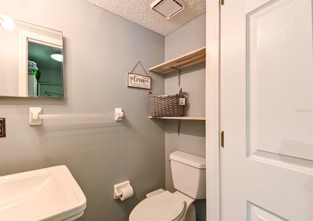 half bath featuring a sink, a textured ceiling, and toilet