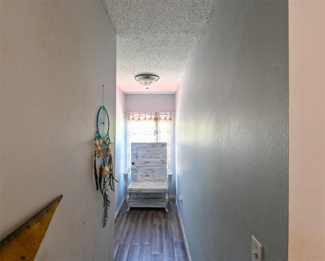 hall with a textured ceiling, a textured wall, wood finished floors, and baseboards