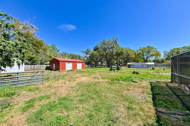 view of yard featuring a detached garage, fence, and an outbuilding