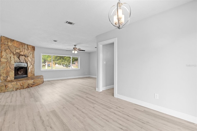unfurnished living room featuring ceiling fan with notable chandelier, light wood-type flooring, a fireplace, baseboards, and visible vents