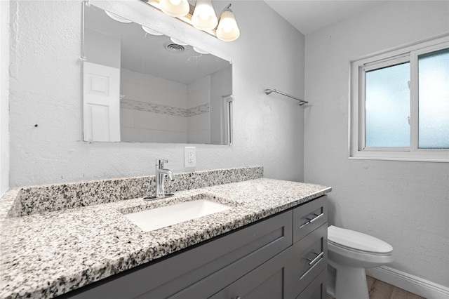 bathroom with toilet, baseboards, wood finished floors, a textured wall, and vanity