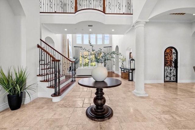 entryway featuring baseboards, stairs, stone tile flooring, a towering ceiling, and arched walkways