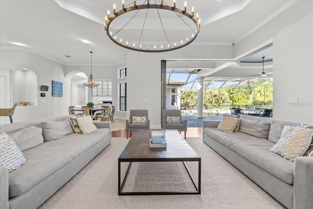 living room featuring ceiling fan with notable chandelier, crown molding, baseboards, and arched walkways