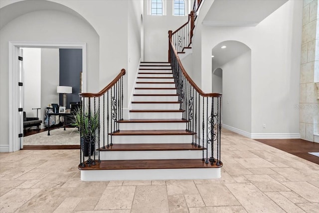 stairway featuring baseboards, arched walkways, stone tile floors, and a towering ceiling