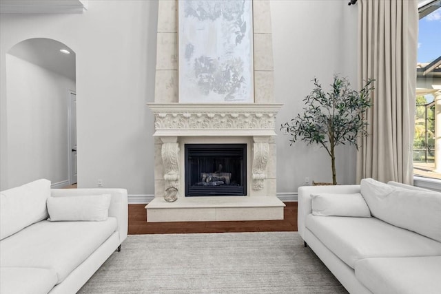 living room with arched walkways, a large fireplace, baseboards, and wood finished floors