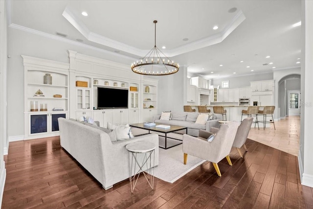 living room featuring a chandelier, a tray ceiling, and dark wood-style flooring