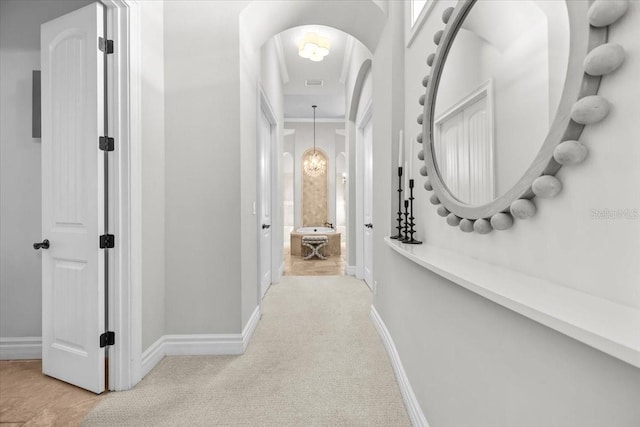 hall with visible vents, a notable chandelier, arched walkways, baseboards, and light colored carpet