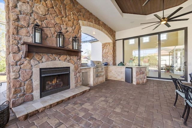 view of patio with ceiling fan, area for grilling, a grill, and an outdoor stone fireplace