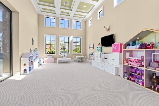 recreation room featuring coffered ceiling, a high ceiling, a healthy amount of sunlight, and carpet