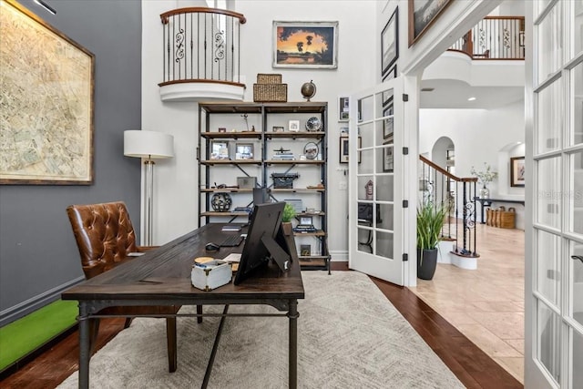 home office featuring wood finished floors, french doors, arched walkways, baseboards, and a towering ceiling