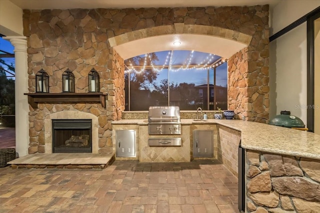 view of patio / terrace featuring a sink, grilling area, an outdoor stone fireplace, and an outdoor kitchen