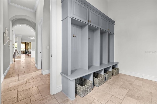 mudroom with stone tile floors, arched walkways, crown molding, and baseboards