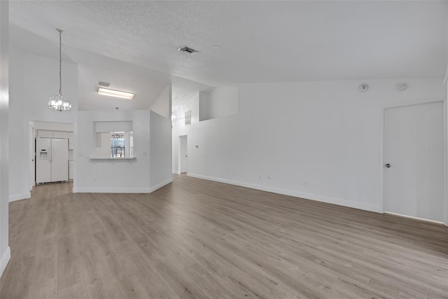 unfurnished living room featuring visible vents, light wood-style flooring, a textured ceiling, baseboards, and lofted ceiling