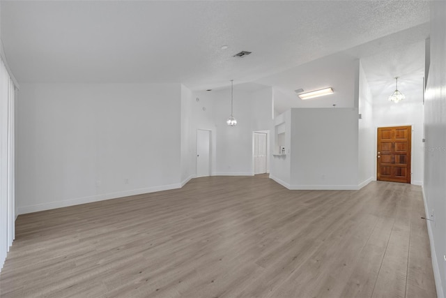 unfurnished living room featuring visible vents, lofted ceiling, light wood-style flooring, a notable chandelier, and a textured ceiling