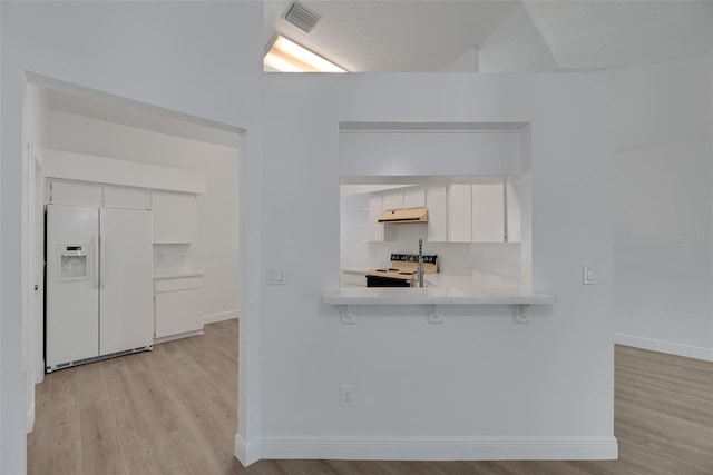 kitchen with under cabinet range hood, light countertops, light wood-style flooring, white appliances, and white cabinetry