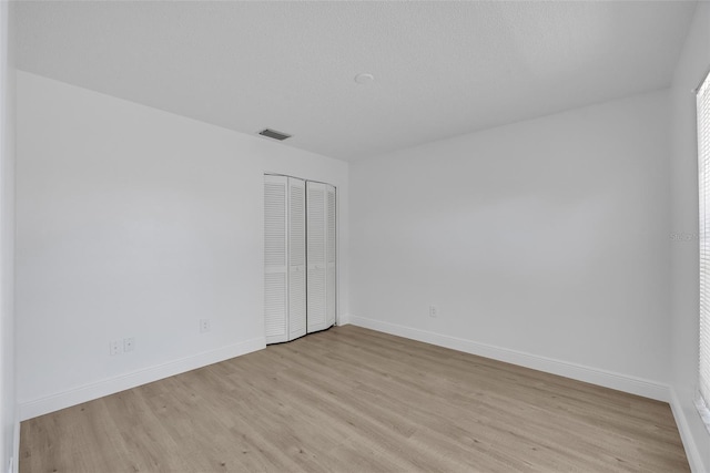 empty room featuring light wood-type flooring, visible vents, baseboards, and a textured ceiling