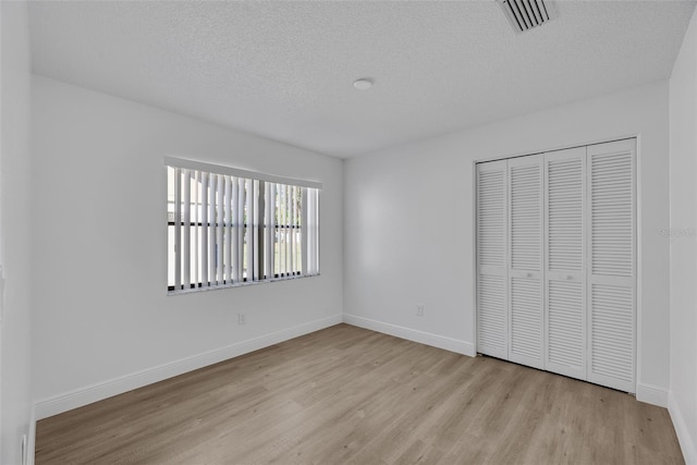 unfurnished bedroom featuring visible vents, baseboards, a closet, and wood finished floors