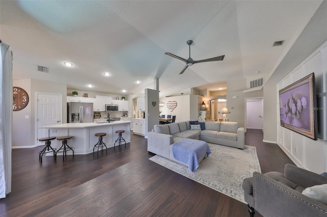 living area featuring visible vents, dark wood finished floors, a ceiling fan, and vaulted ceiling