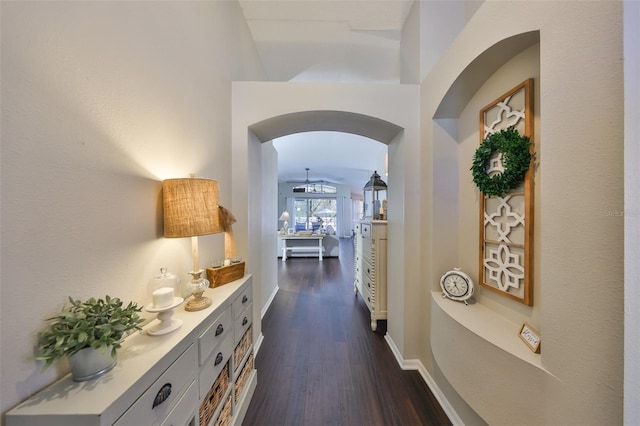 hallway with arched walkways, dark wood-type flooring, and baseboards