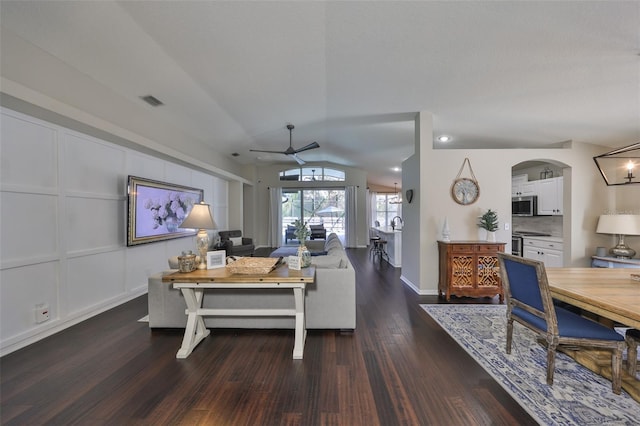 living area with ceiling fan, vaulted ceiling, wood finished floors, arched walkways, and a decorative wall