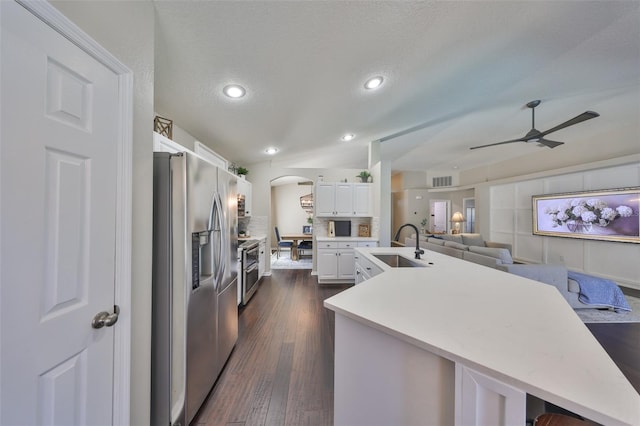 kitchen with dark wood finished floors, appliances with stainless steel finishes, arched walkways, white cabinetry, and a sink