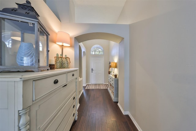 entryway with arched walkways, dark wood finished floors, and baseboards