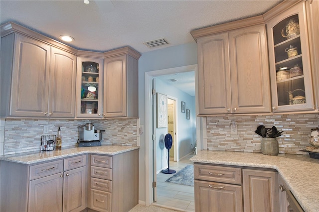 kitchen with light stone counters, visible vents, baseboards, decorative backsplash, and glass insert cabinets