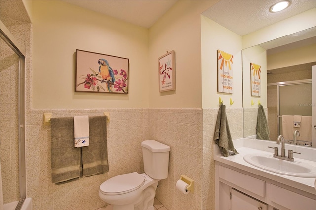 full bath featuring toilet, a stall shower, tile walls, wainscoting, and vanity