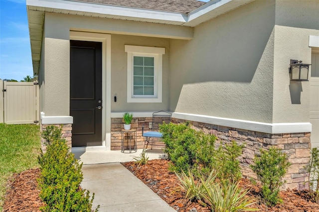 property entrance featuring stone siding, roof with shingles, and stucco siding