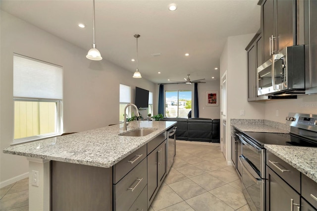 kitchen featuring light stone counters, an island with sink, a sink, appliances with stainless steel finishes, and open floor plan