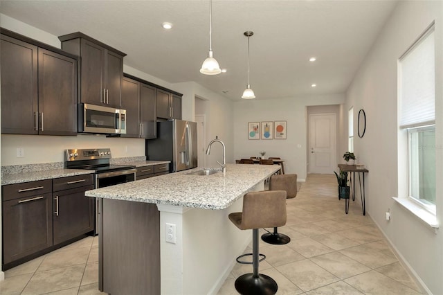 kitchen featuring a center island with sink, a breakfast bar, a sink, dark brown cabinetry, and appliances with stainless steel finishes