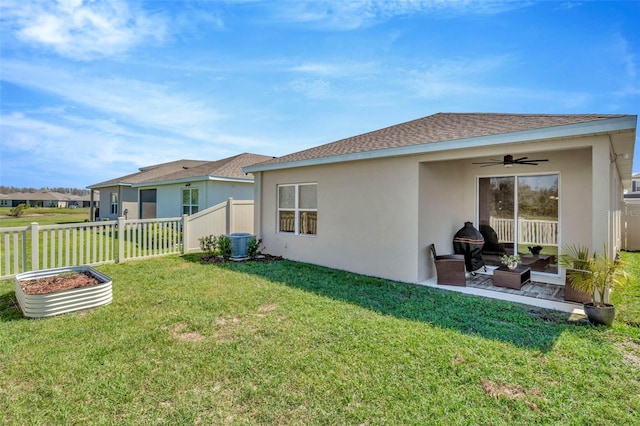 rear view of property with stucco siding, fence, a yard, a shingled roof, and ceiling fan