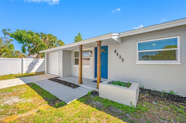 doorway to property featuring covered porch, fence, driveway, and stucco siding