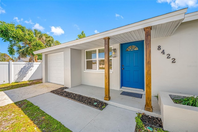 property entrance featuring a garage, driveway, covered porch, fence, and stucco siding