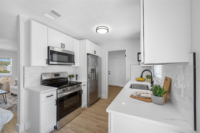 kitchen featuring light wood finished floors, visible vents, appliances with stainless steel finishes, a sink, and backsplash