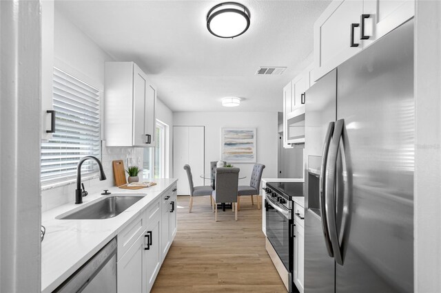 kitchen with stainless steel appliances, visible vents, light wood-style flooring, white cabinets, and a sink