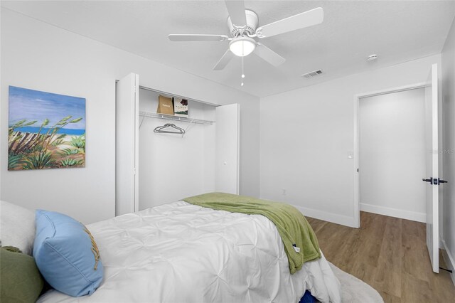 bedroom with baseboards, visible vents, ceiling fan, wood finished floors, and a closet