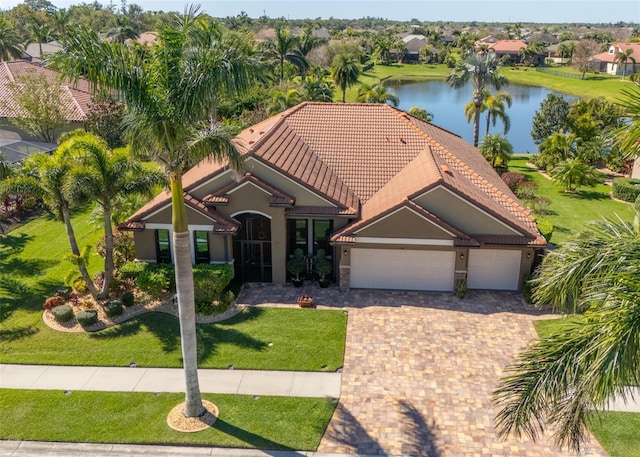 mediterranean / spanish house featuring a front lawn, a water view, a tile roof, driveway, and an attached garage