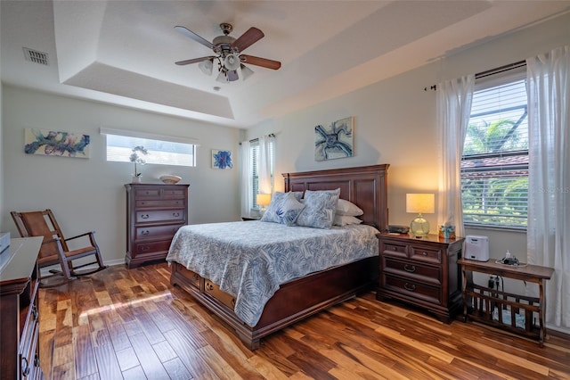 bedroom featuring visible vents, wood finished floors, baseboards, a raised ceiling, and ceiling fan