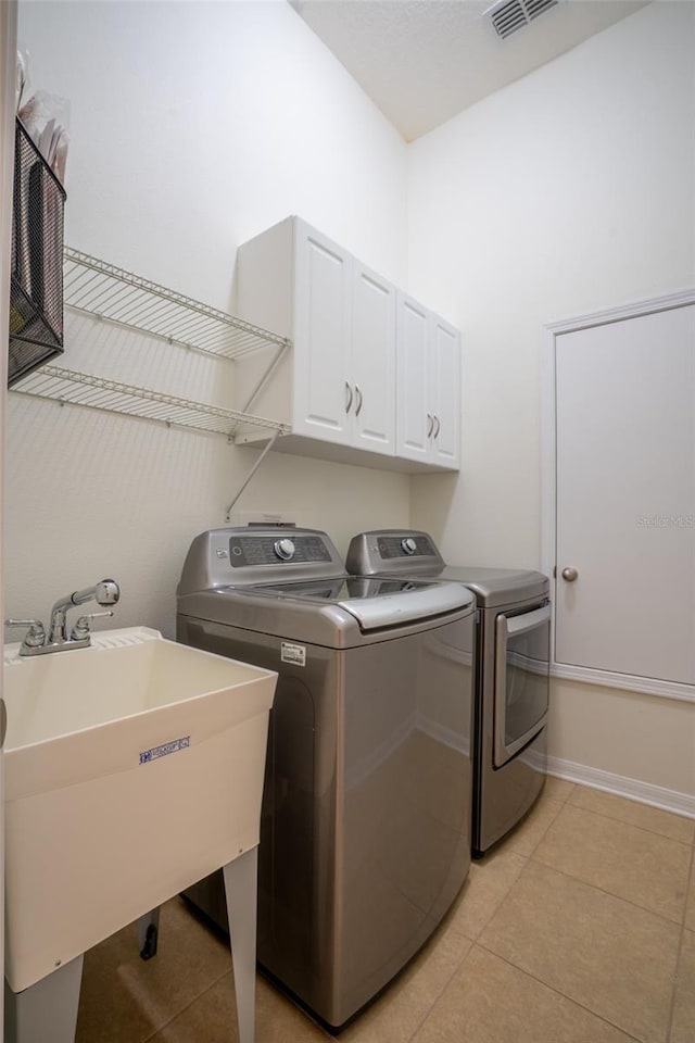 laundry area with visible vents, washing machine and dryer, light tile patterned floors, cabinet space, and a sink