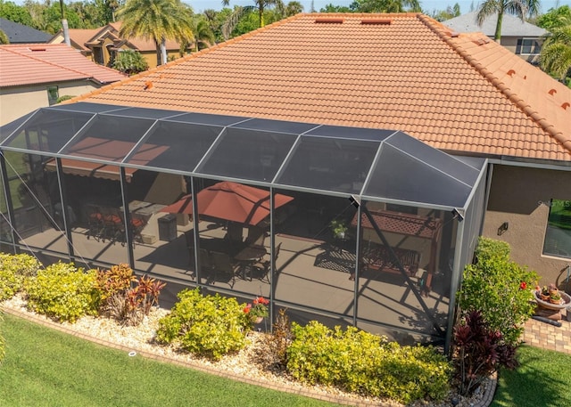 back of house with glass enclosure, a tile roof, and stucco siding