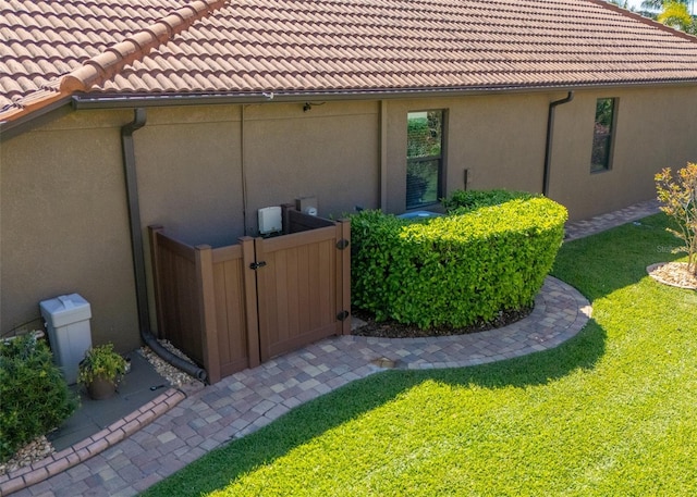 view of property exterior with a gate, stucco siding, a lawn, and a tiled roof