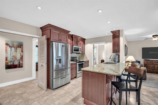 kitchen with a sink, stainless steel appliances, a peninsula, a breakfast bar area, and light stone countertops