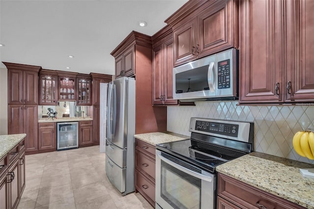 kitchen featuring tasteful backsplash, glass insert cabinets, wine cooler, light stone counters, and stainless steel appliances