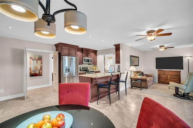 kitchen with a kitchen bar, a ceiling fan, appliances with stainless steel finishes, a peninsula, and light stone countertops