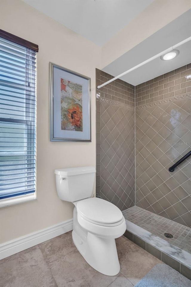 full bathroom with a tile shower, baseboards, toilet, and a wealth of natural light