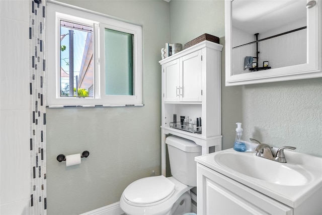 bathroom featuring vanity, toilet, a textured wall, and baseboards