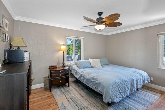 bedroom featuring light wood-style flooring, crown molding, baseboards, and ceiling fan