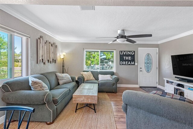 living room with plenty of natural light, ornamental molding, visible vents, and wood finished floors