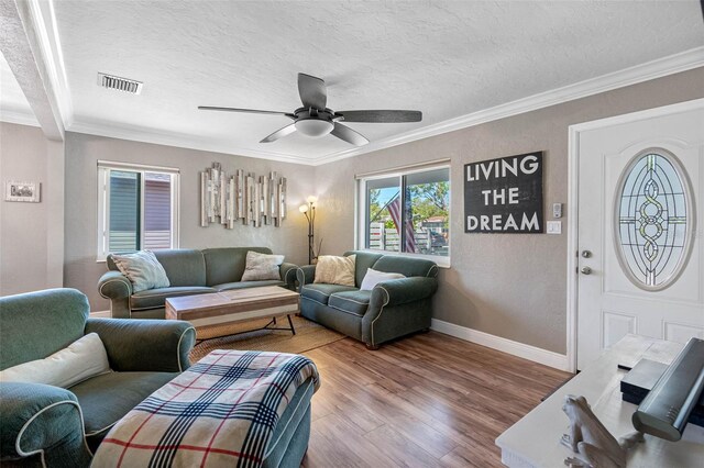 living room featuring ornamental molding, wood finished floors, visible vents, and a textured ceiling